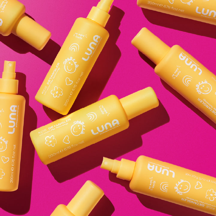 Yellow bottles of LUNA Pro Haircare Kids Detangling Spray on a pink background